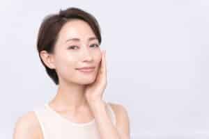 A woman smiling and touching her cheek after Restylane® treatments in Miami