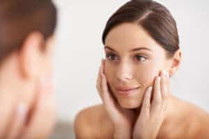 A woman looking in the mirror after rhinoplasty in Miami