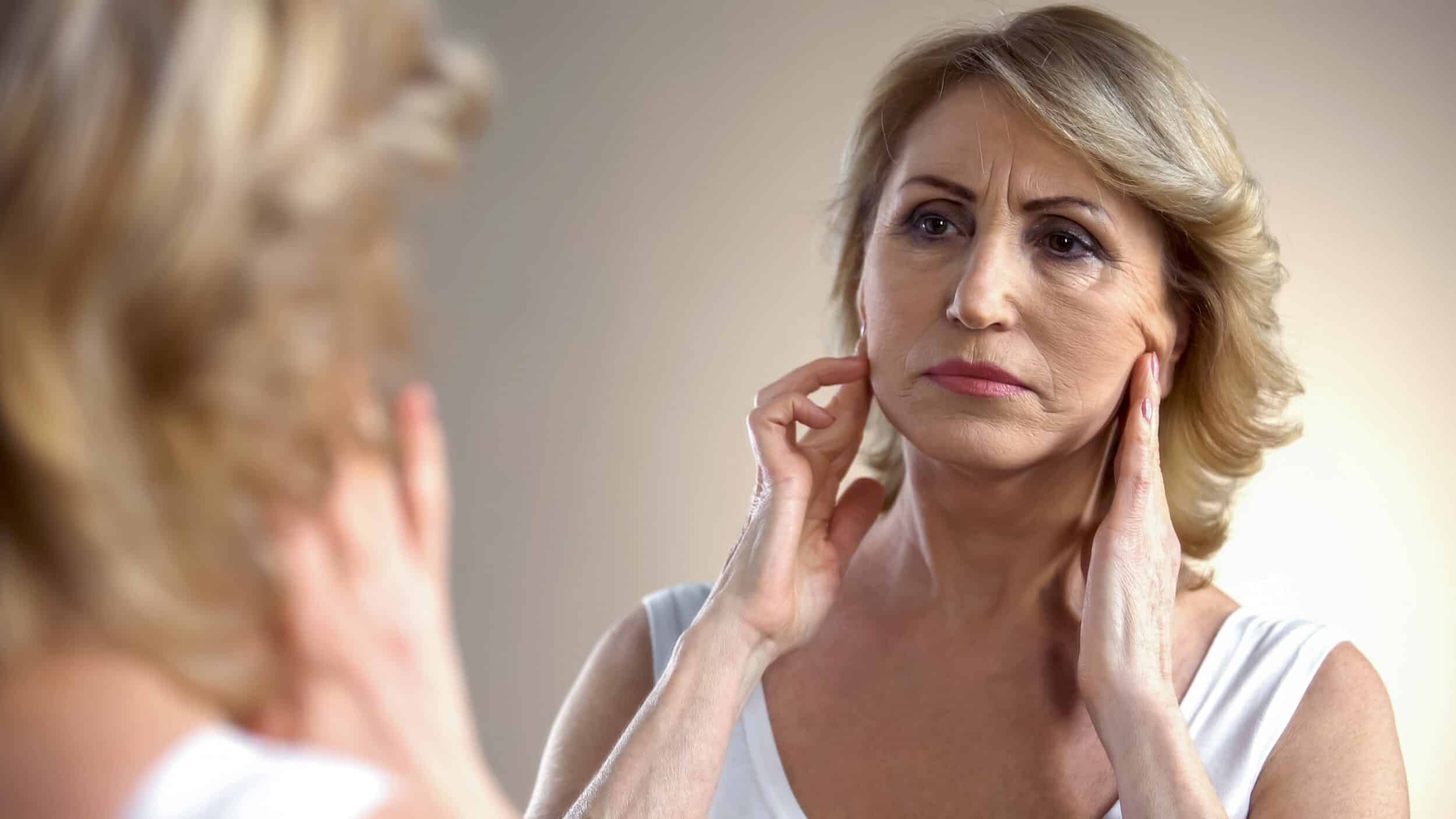 A woman looking in the mirror and considering a facelift in Miami