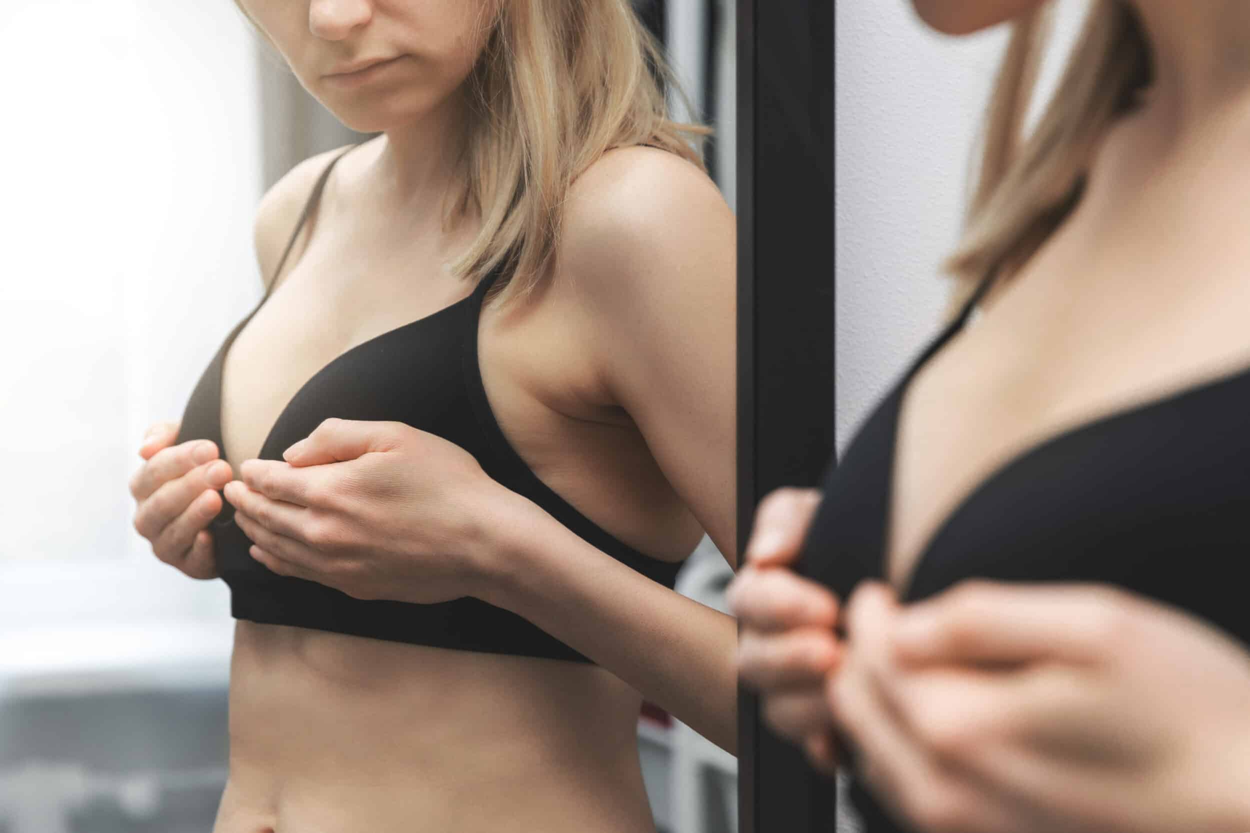 A cropped shot of a woman in a black bra looking in the mirror after breast reduction in Miami